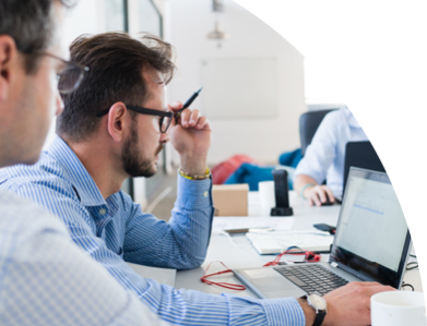 Eine Gruppe von Menschen sitzt am Schreibtisch und blicken konzentriert auf ihre Laptops.